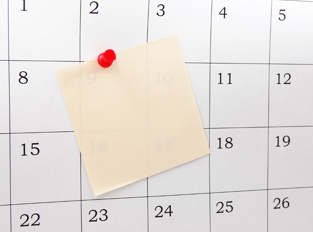 Calendário com um post-it em branco preso por um alfinete vermelho, cobrindo parcialmente alguns números das datas.
